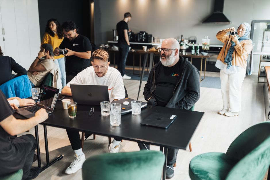 A diverse group of adults working collaboratively in a modern office with laptops and drinks on the table.