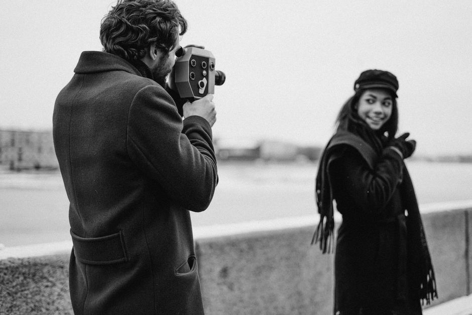 A man filming a woman outdoors with a vintage camera in monochrome style.