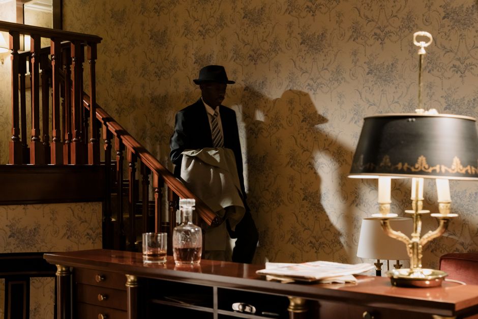 A shadowy detective in vintage attire descends wooden stairs, evoking a classic noir mood.