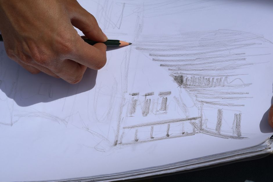 Artist sketching a building in a sketchbook outdoors, showcasing urban architecture.