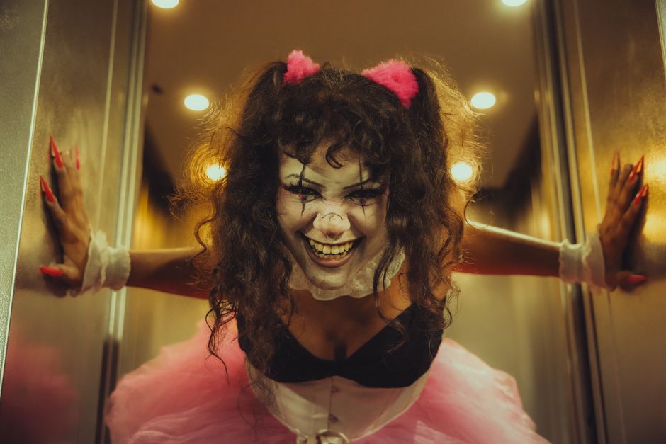 A spooky clown in an elevator with dramatic lighting, wearing a pink tutu and scary makeup.
