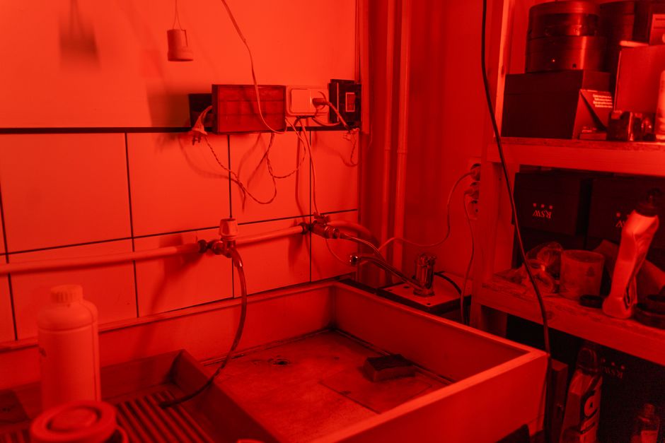 An atmospheric darkroom setup featuring a washbasin and red ambient lighting for processing photos.