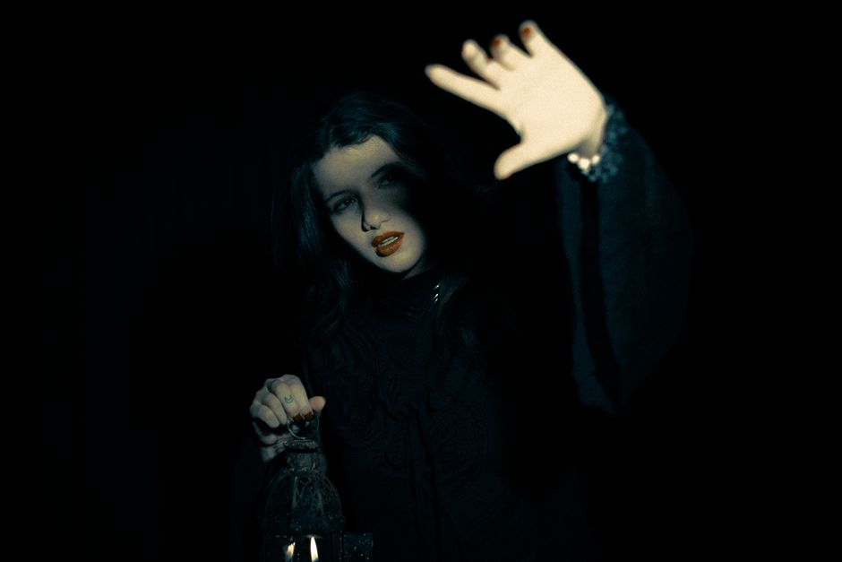 An enigmatic woman surrounded by darkness, holding a lantern, creating a mysterious atmosphere.