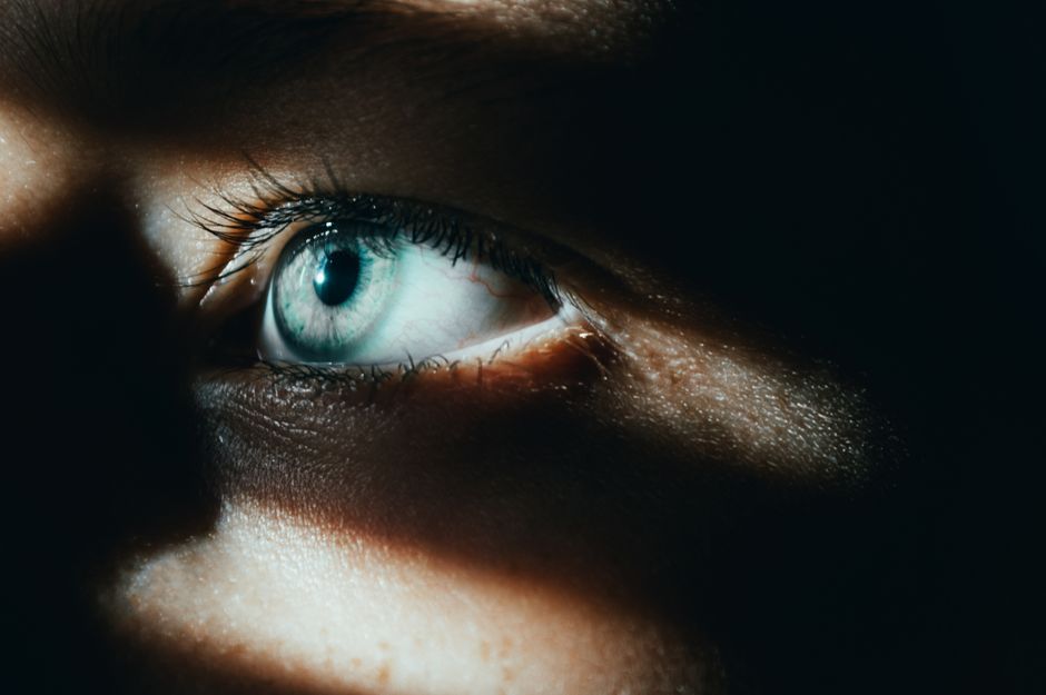 A dramatic and moody close-up of a blue eye in shadow, highlighting detail.