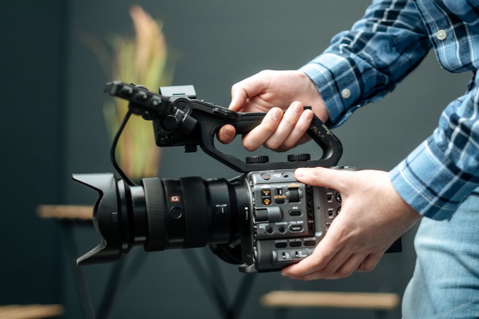 Detailed close-up of hands operating a professional video camera indoors. Ideal for media-related content.