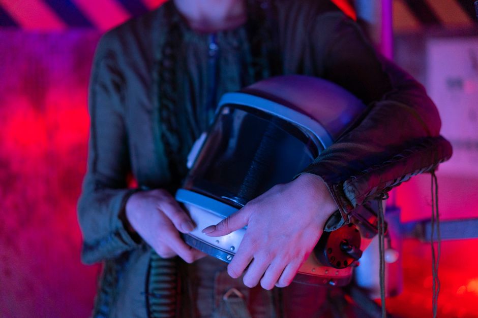 A person holding an astronaut helmet with neon lighting in a sci-fi setting.
