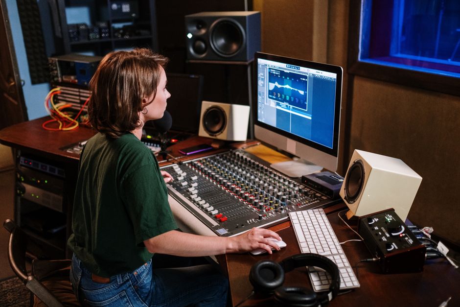 Woman in studio working on sound mixer and computer, focused on audio editing.