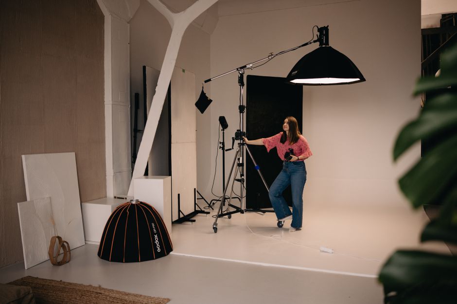 Female photographer setting up lighting in a modern studio environment with tripods and equipment.