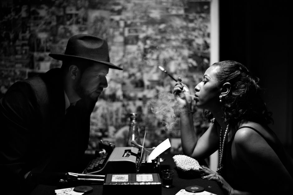 Dramatic black and white vintage scene with a smoking woman and a man in a hat.