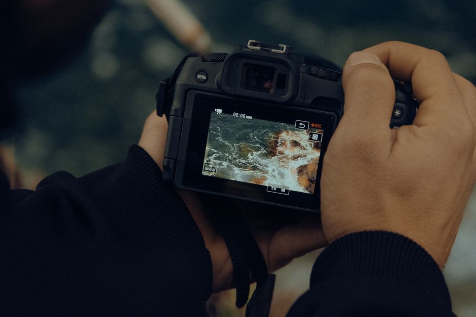 A close-up of a digital camera screen displaying a video of ocean waves crashing on rocks.
