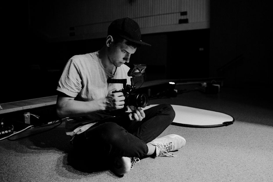 A man with a camera sits cross-legged, focusing intently in a studio setting.