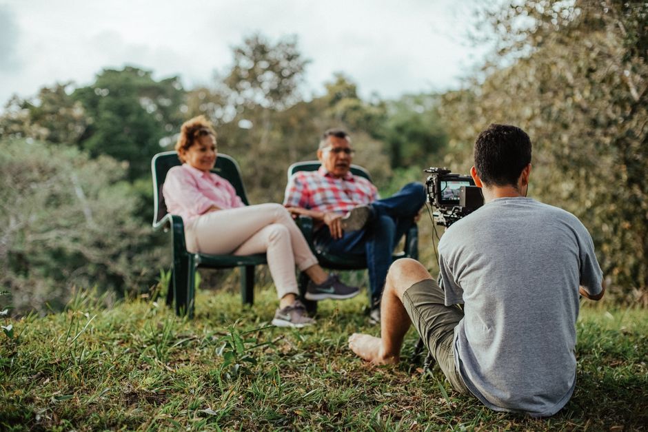 A couple being interviewed outdoors by a photographer in a lush garden setting.