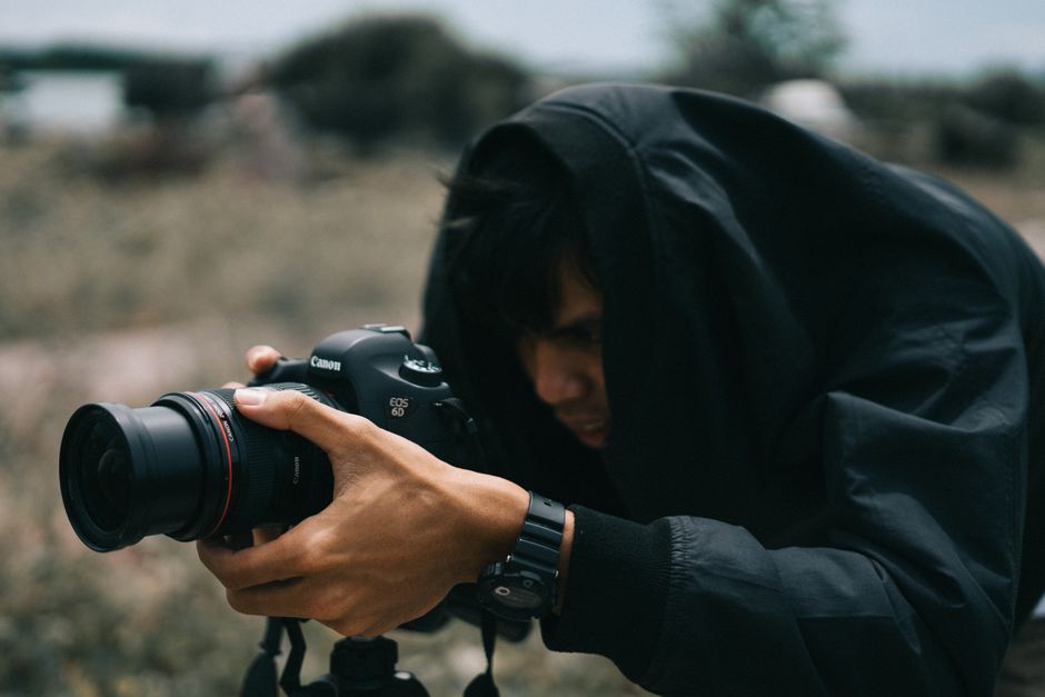 A photographer focused outdoors, capturing moments with a camera, wrapped in a dark coat.
