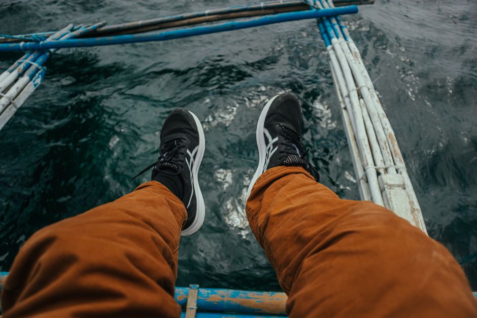 A person sitting on a boat with legs hanging over water, showcasing a peaceful travel moment.
