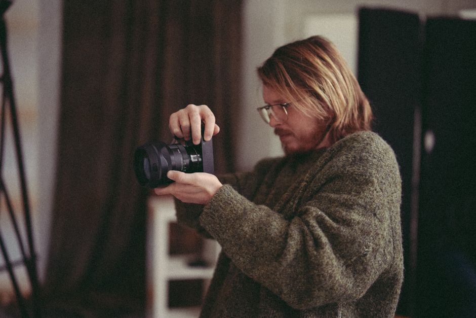 A male photographer intently adjusting his camera to take a high-quality photograph indoors.