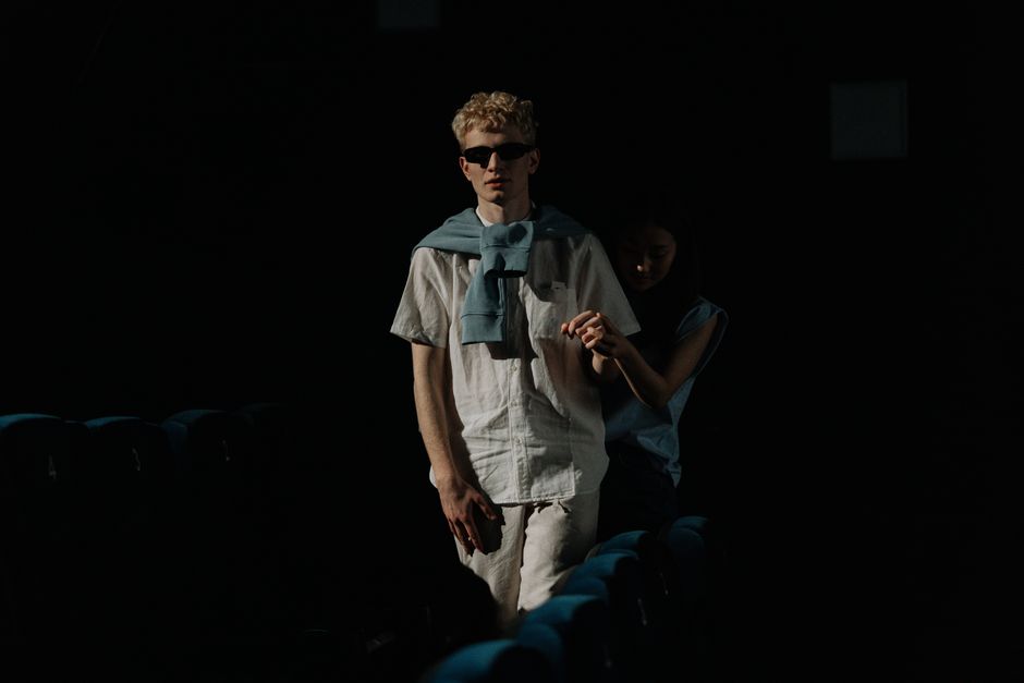 A visually impaired man with guide navigating through a dark movie theater.