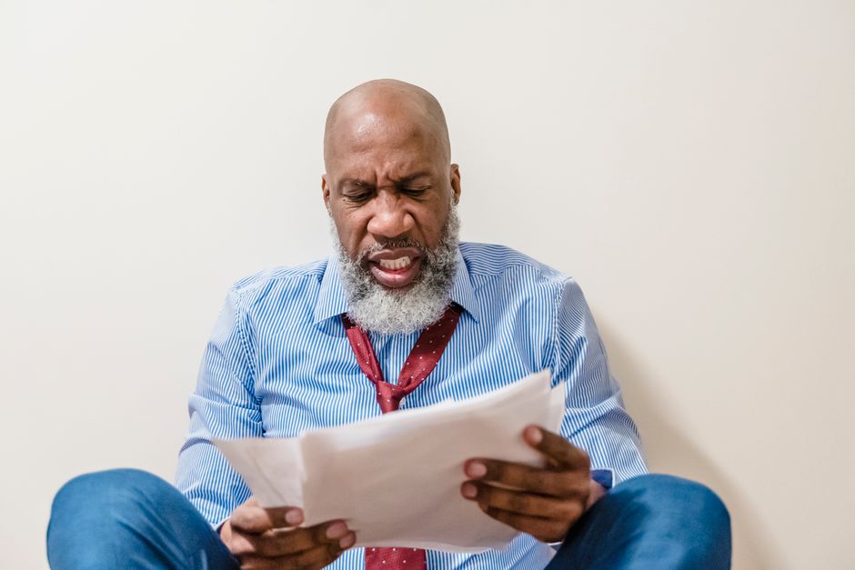 Bald African American man looking stressed while reading documents indoors.