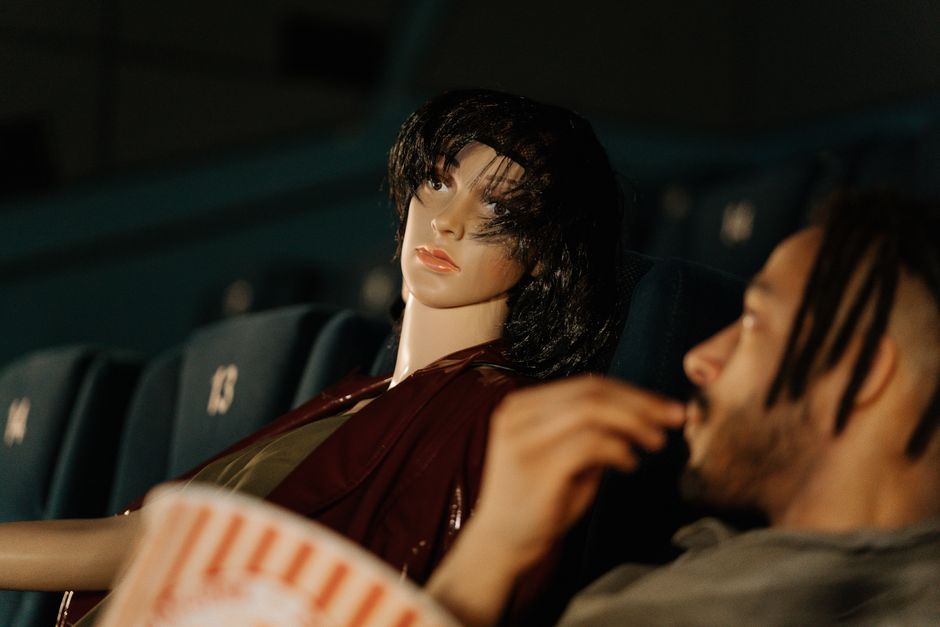A man and a mannequin watching a movie in a theater, creating a conceptual scene.