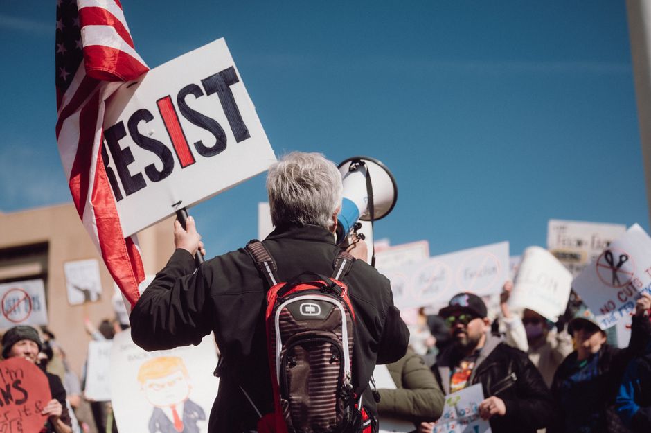 Crowd at a rally holding signs with a strong message of resistance.