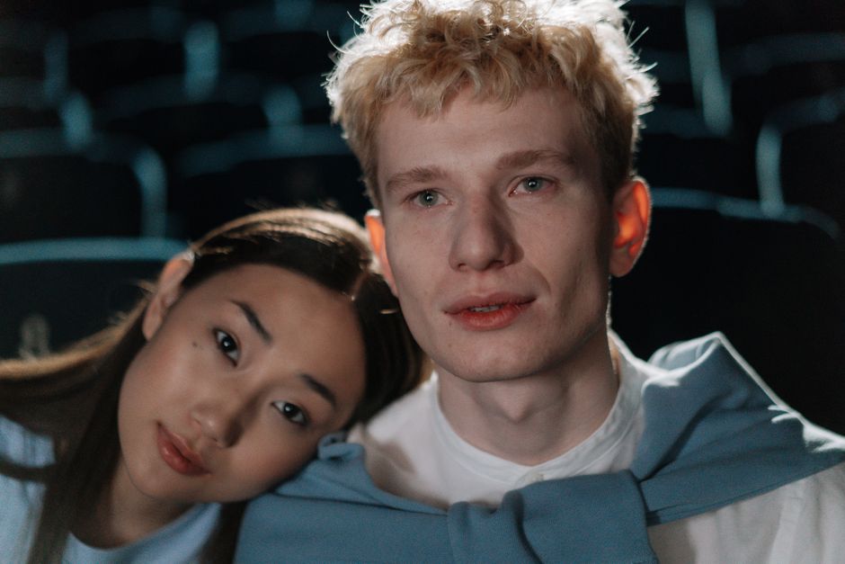 Close-up of a multicultural couple in a dimly lit theater, sharing a quiet moment.