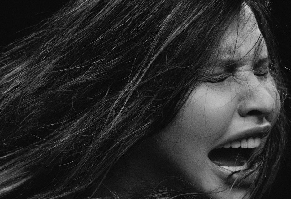 Dramatic black and white close-up of a woman's face with eyes closed and hair blowing, expressing strong emotion.