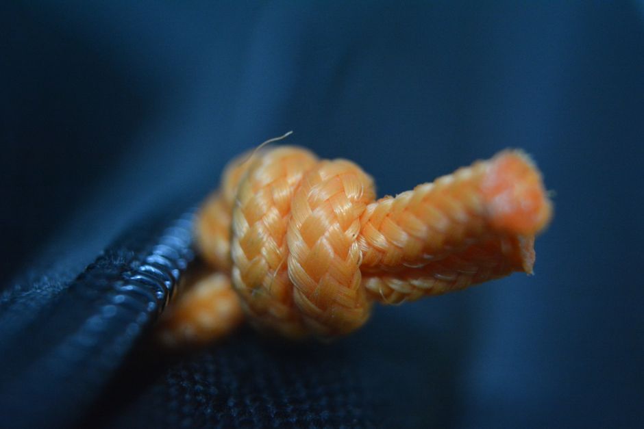Detailed close-up of an orange rope knot against a dark background, showcasing texture.