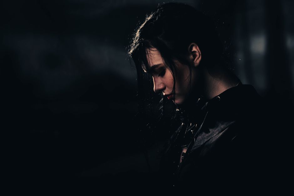 A dramatic portrait of a woman with black hair in a dark setting, evoking mystery and contemplation.