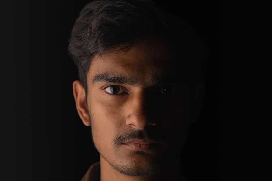 Close-up portrait of a young male model with shadowed face and intense gaze.
