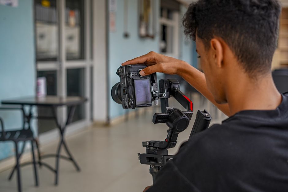 A photographer adjusts a DSLR camera on a stabilizer indoors, focusing on the setup.