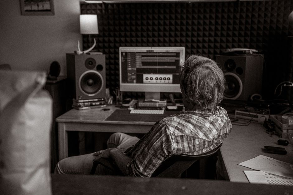 A man sits at a computer in a soundproof studio editing audio on a screen.