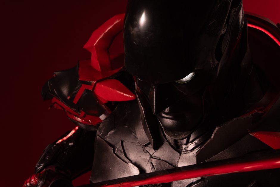 Close-up of a character in an intricate red and black cosplay costume, illuminated dramatically.