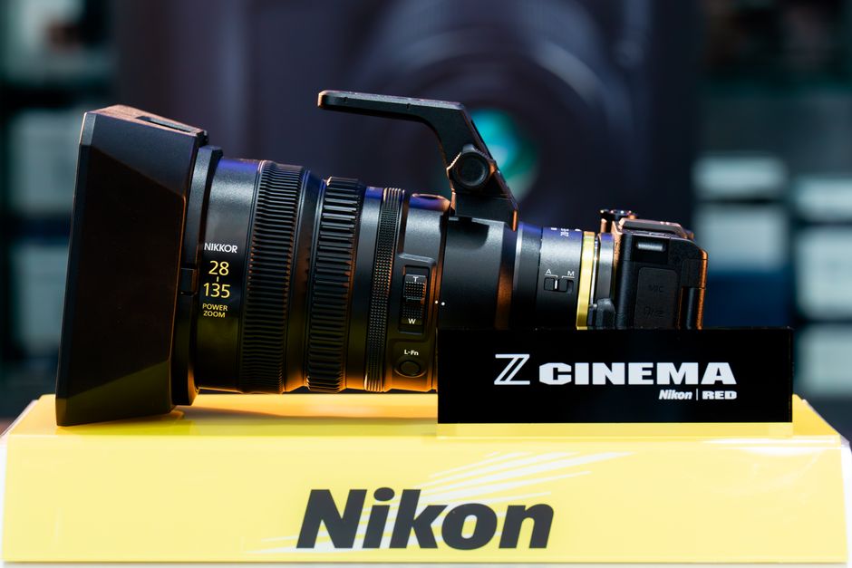 Side view of a professional cinema camera lens by Nikon on a display stand at an expo.