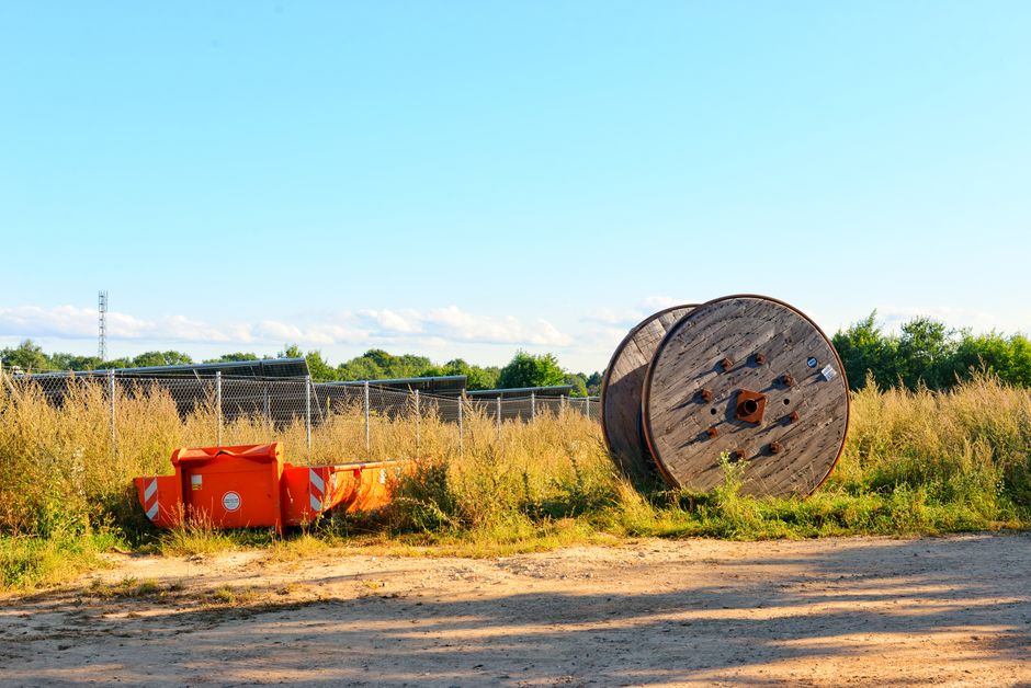 An outdoor scene featuring a large wooden spool and orange construction barriers against a sunny blue sky.