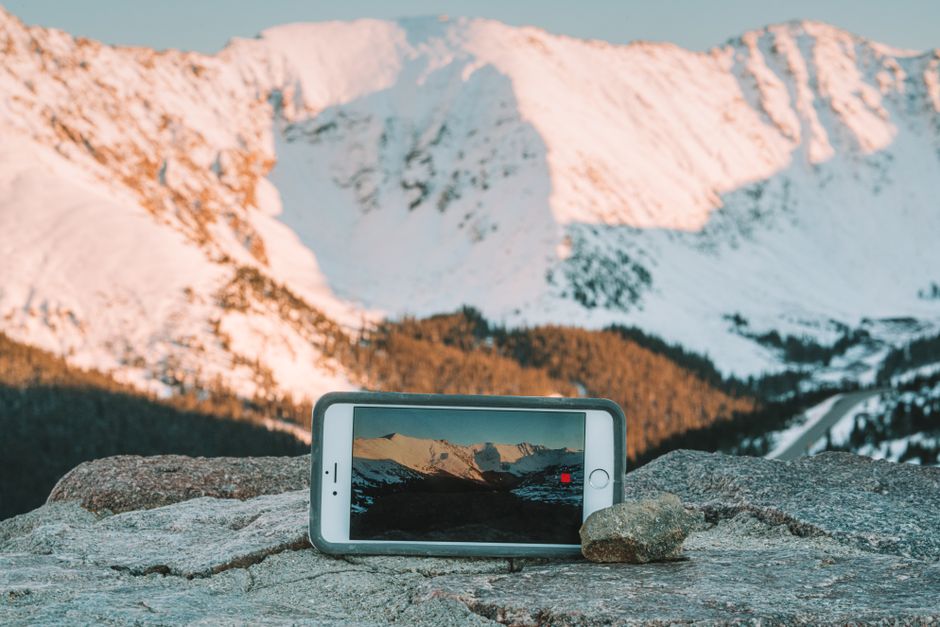A smartphone recording a snowy mountain sunset scene, showcasing a winter wonderland.