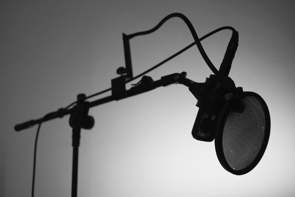 Black and white image of a professional studio microphone with a boom arm and pop filter.