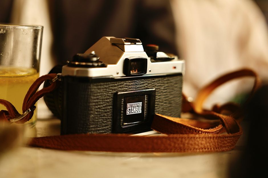 A vintage film camera with a leather strap sits beside a glass of orange juice on a table.