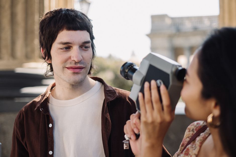 A young man and woman using a vintage movie camera near a colonnade, enjoying outdoor filmmaking.