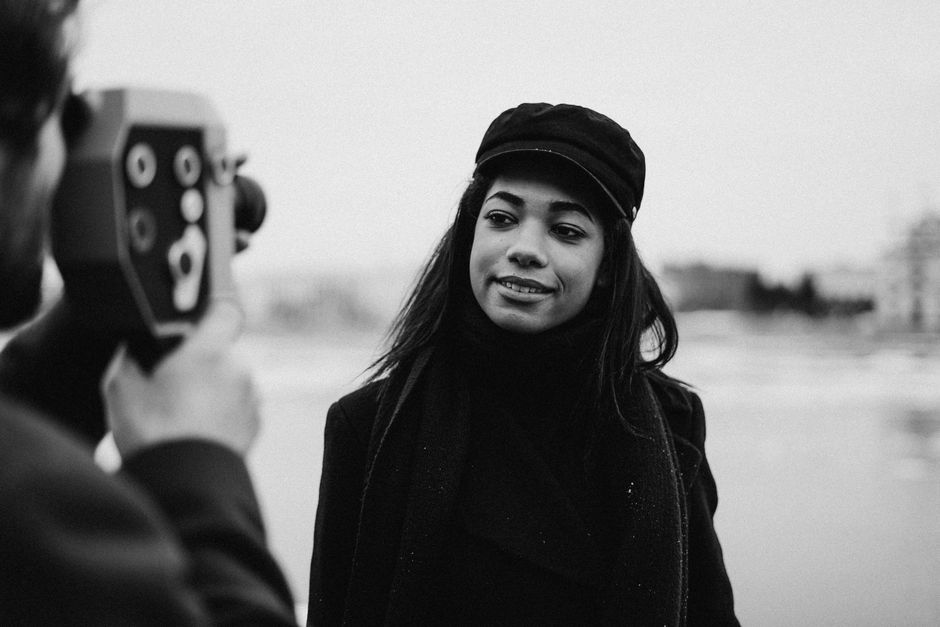 Black and white portrait of a woman smiling while being filmed outdoors.