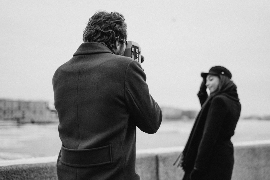 Black and white photo of a man filming a woman outdoors.
