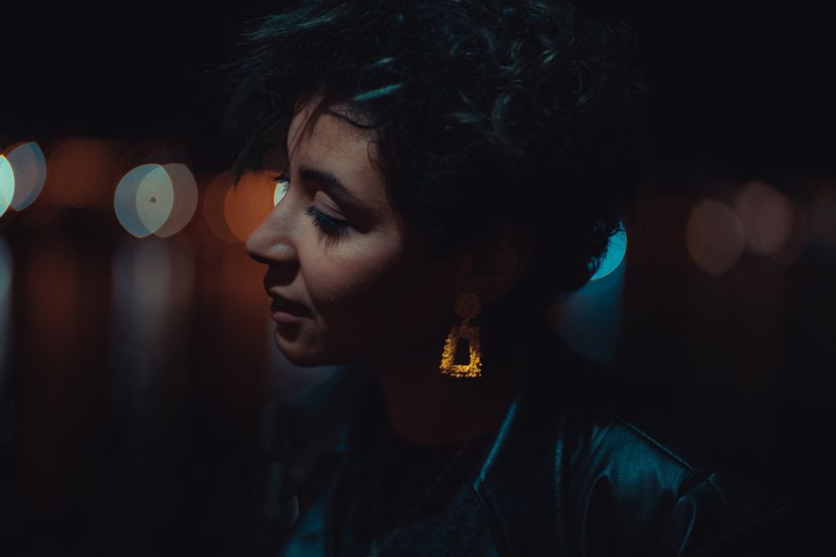 Side profile of a woman with short hair and striking earrings, captured in bokeh lighting at night.