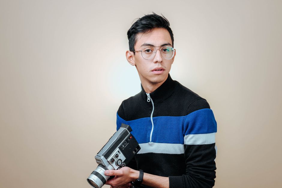 Portrait of a man with glasses holding a vintage camera in a studio setting.