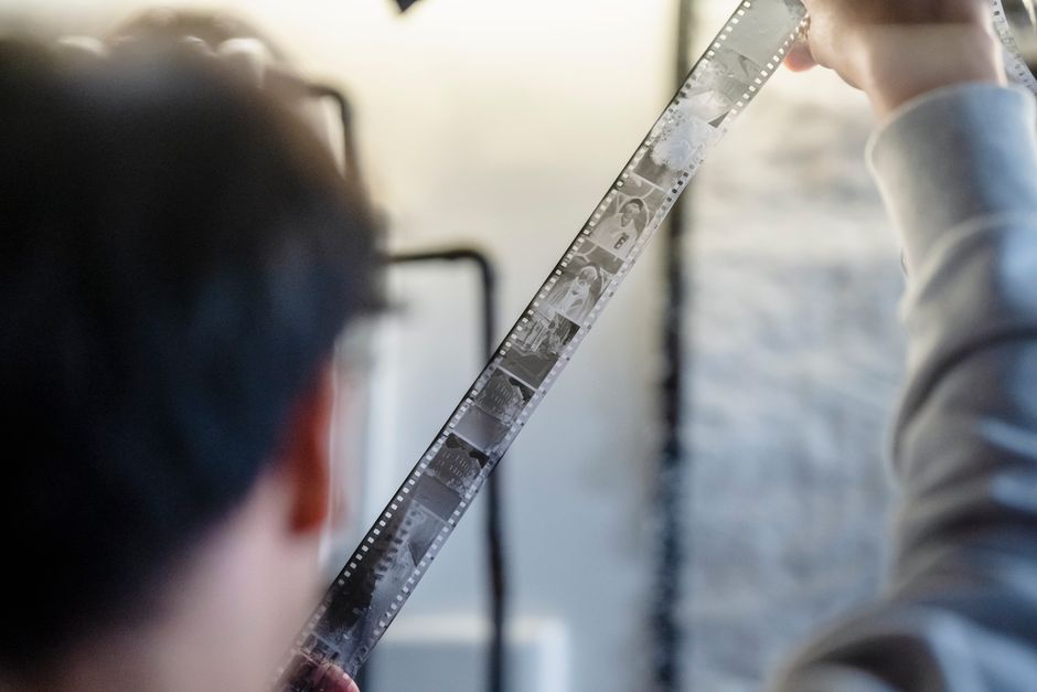 Adult examining a film strip indoors with focused attention on details and imagery.