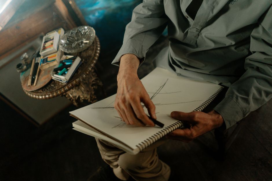 Close-up of an artist sketching with charcoal on paper in a cozy, indoor workspace.