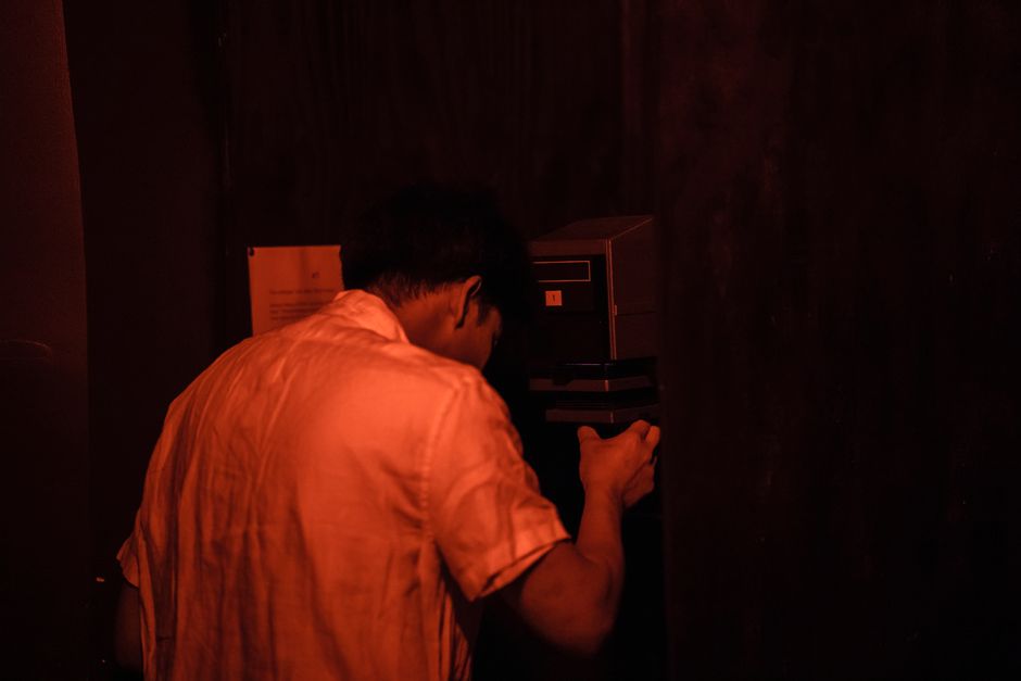 A man in a dimly lit darkroom, focused on the film development process.