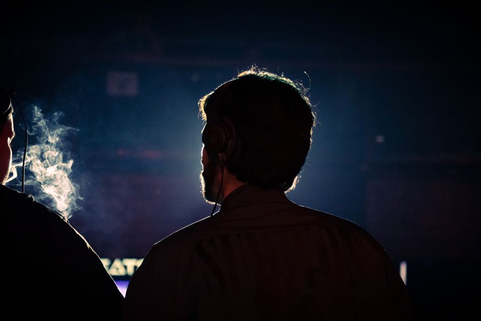 Dark, moody silhouette of a DJ with headphones in a smoky room, capturing a mysterious nightlife vibe.