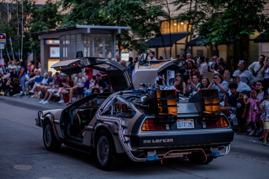 A DeLorean car at a street parade in Minneapolis with a crowd watching.