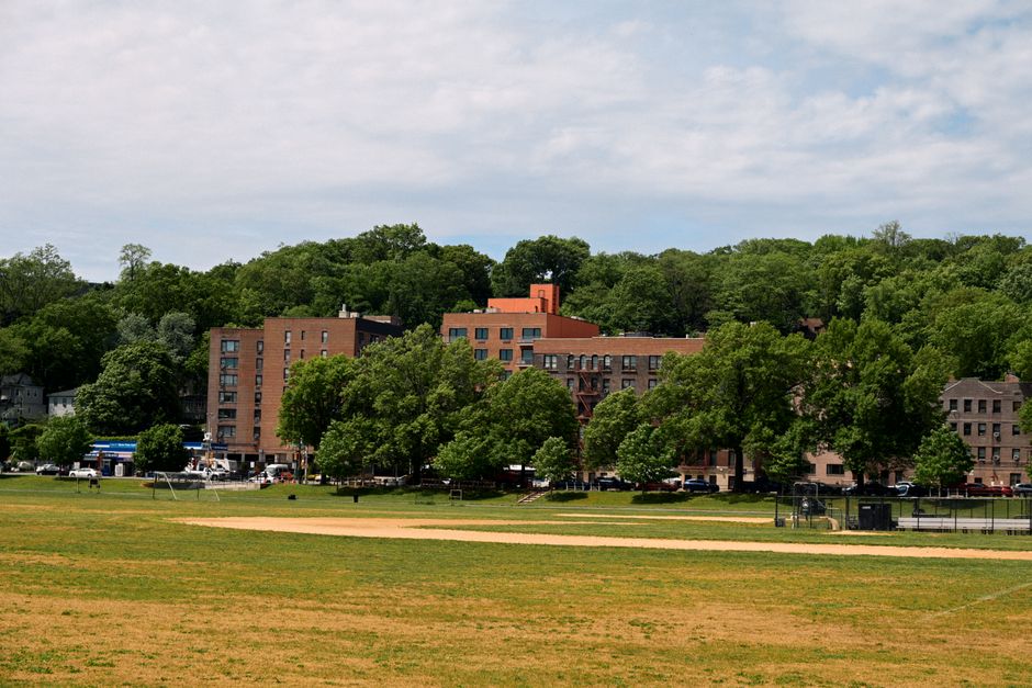 A scenic view of a park with residential buildings and lush trees under a cloudy sky.