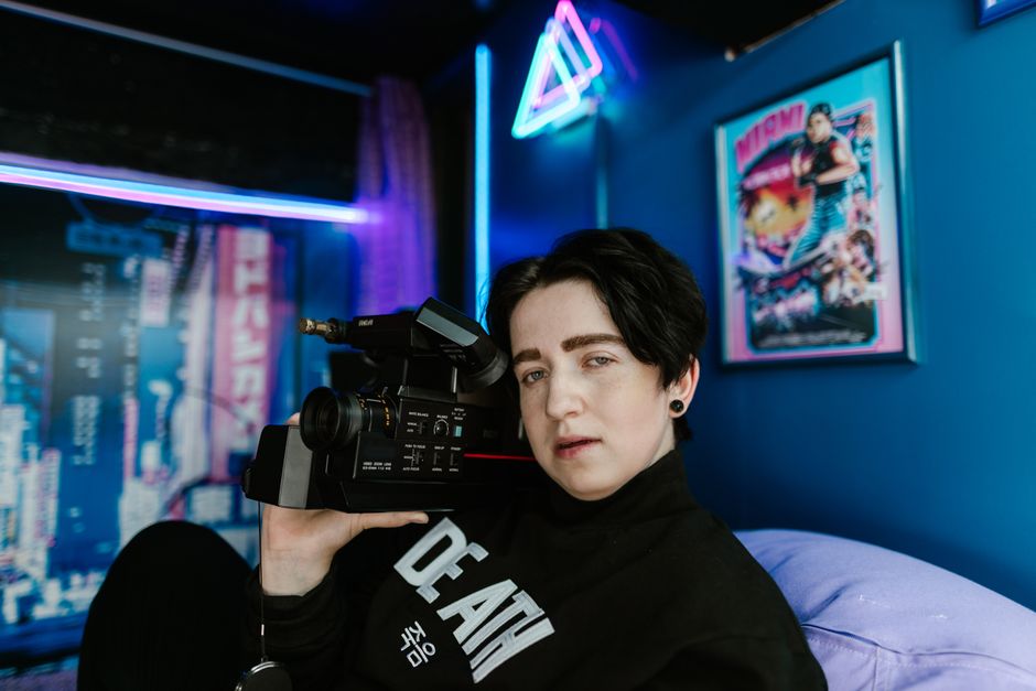 Portrait of a person holding a vintage camcorder in a neon-lit room, capturing a retro vibe.