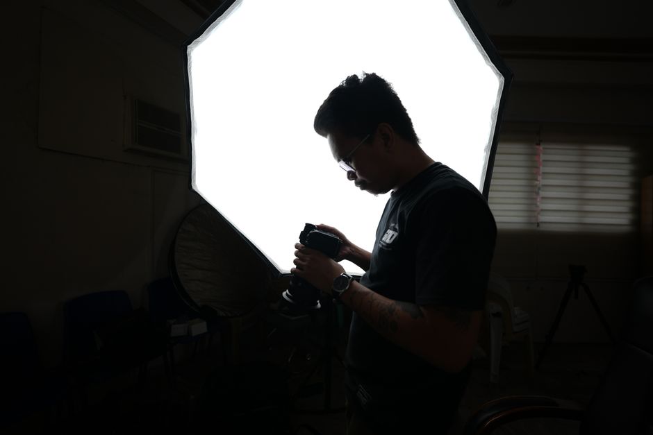 Professional photographer adjusting camera settings in a dimly lit studio with softbox lighting.