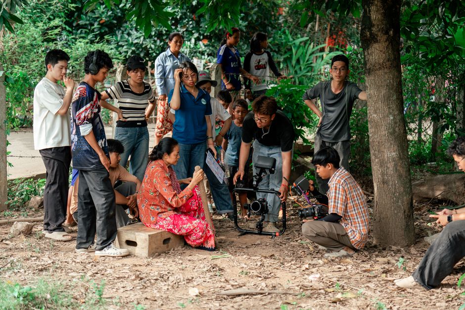 Filmmakers and crew collaborate on outdoor movie set under trees.